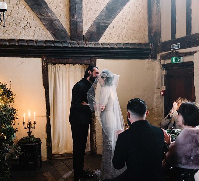 Bride wearing vintage styled floral headpiece with corset waist dress and groom in black suit tie the knot