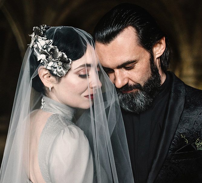 Bride wearing silver gothic styled dress with corset waist, cob-web train and groom in black suit and shirt