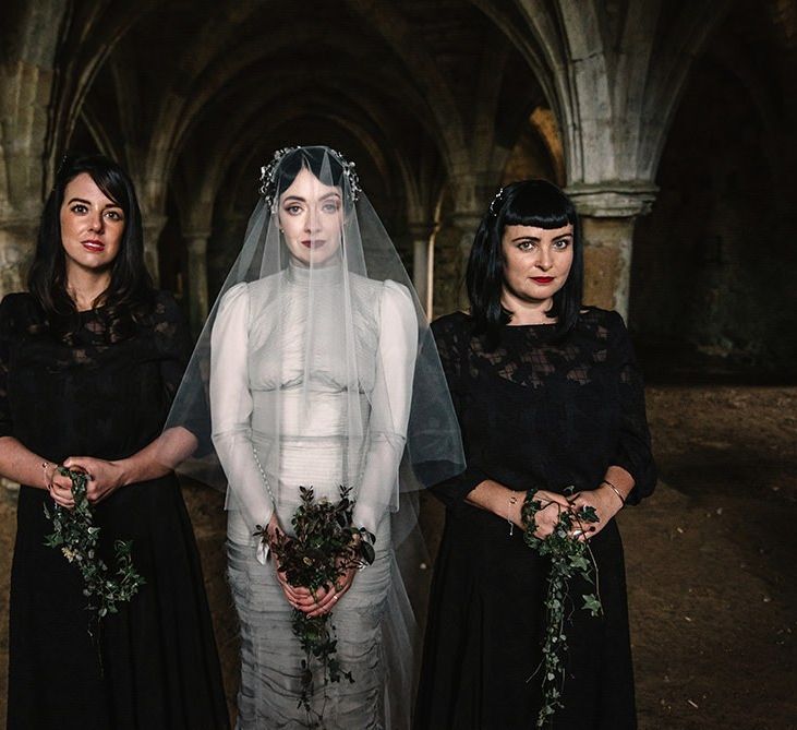 Bride wearing silver dress and bridesmaids in black dress with foliage bouquets