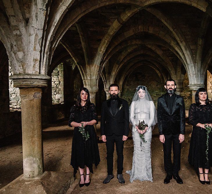 Bride wearing silver dress and bridesmaids in black dress with foliage bouquets for gothic wedding