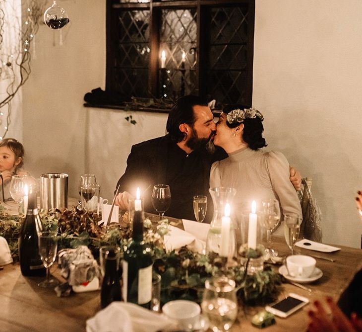 Bride and groom embrace wearing silver dress, vintage floral headpiece and black suit