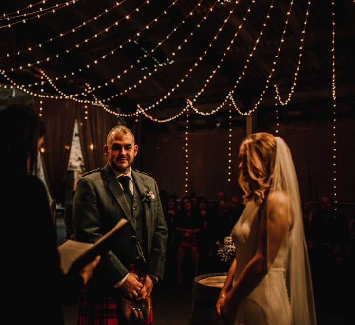 Bride in Anne Priscilla Signature Gown with Halterneck, Keyhole Back and Belt | Floor Length Veil | Groom in Family Mackintosh Tartan Kilt | Kinkell Byre Wedding Venue | Festoon Light Canopy and Indoor Trees for Humanist Wedding in St Andrews | Carla Blain Photography