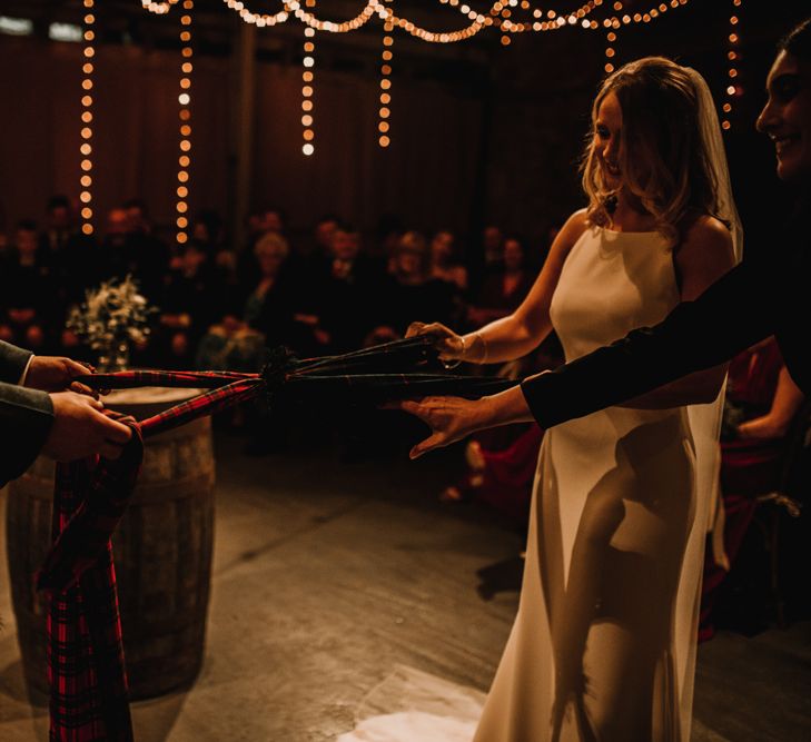 Bride in Anne Priscilla Signature Gown with Halterneck, Keyhole Back and Belt | Floor Length Veil | Groom in Mackintosh Tartan Red and Black Kilt with Green Jacket and Waistcoat | Kinkell Byre Wedding Venue | Festoon Light Canopy and Indoor Trees for Humanist Wedding in St Andrews | Carla Blain Photography