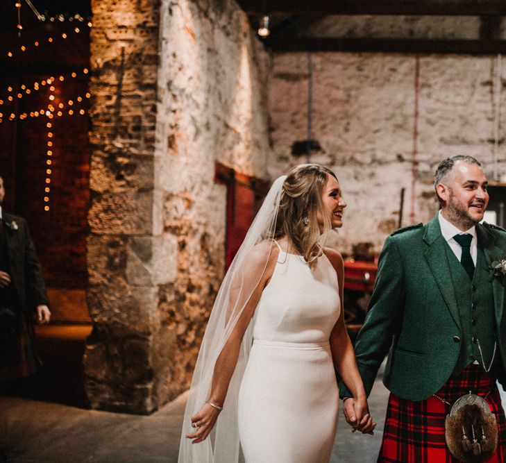 Bride in Anne Priscilla Signature Gown with Halterneck, Keyhole Back and Belt | Floor Length Veil | Groom in Mackintosh Tartan Red and Black Kilt with Green Jacket and Waistcoat | Kinkell Byre Wedding Venue | Festoon Light Canopy and Indoor Trees for Humanist Wedding in St Andrews | Carla Blain Photography