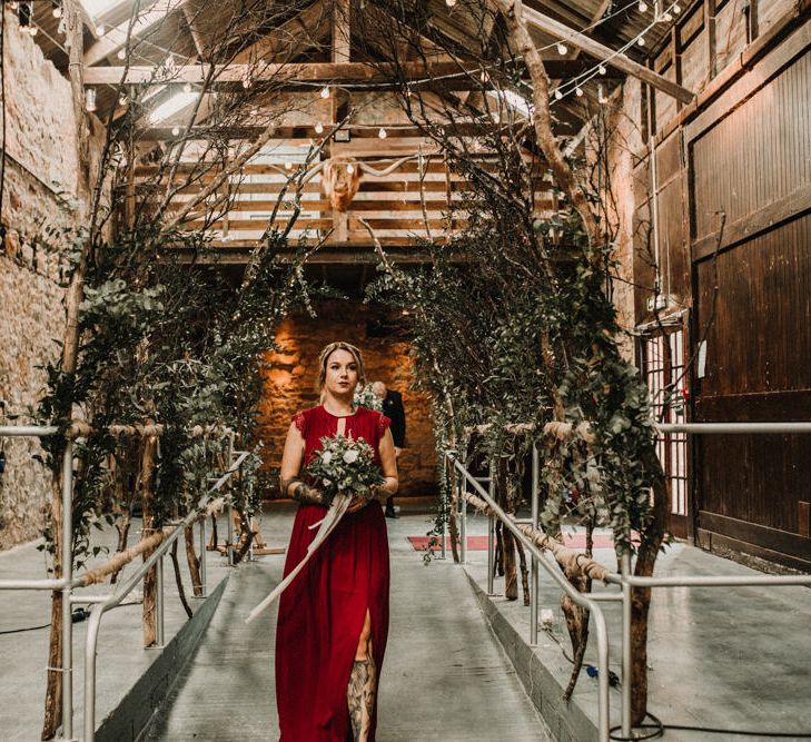 Aisle of Trees | Bridesmaid in Maroon ASOS Dress with Lace Cap Sleeves, Halterneck and Leg Split | Wedding Bouquet of White Flowers and Green Foliage with White Trailing Ribbon | Kinkell Byre Wedding Venue | Festoon Light Canopy and Indoor Trees for Humanist Wedding in St Andrews | Carla Blain Photography