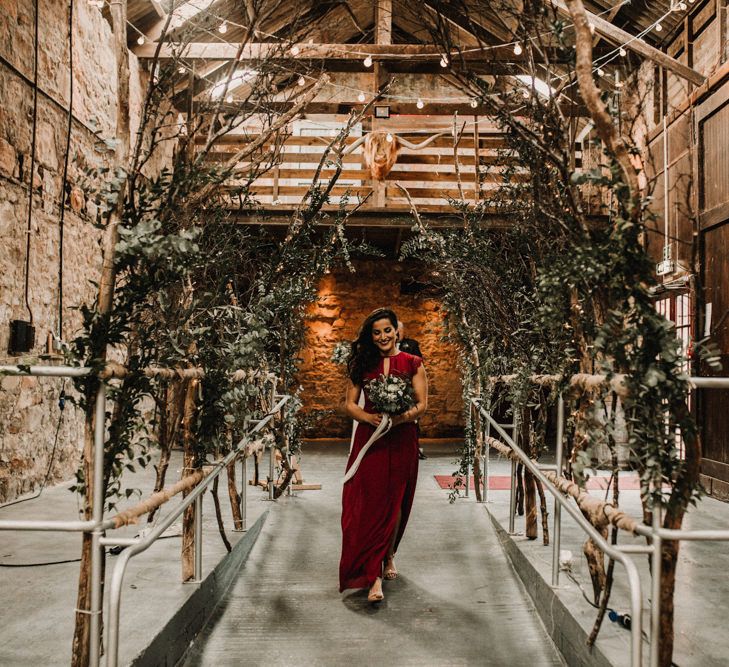 Aisle of Trees | Bridesmaid in Maroon ASOS Dress with Lace Cap Sleeves, Halterneck and Leg Split | Wedding Bouquet of White Flowers and Green Foliage with White Trailing Ribbon | Kinkell Byre Wedding Venue | Festoon Light Canopy and Indoor Trees for Humanist Wedding in St Andrews | Carla Blain Photography