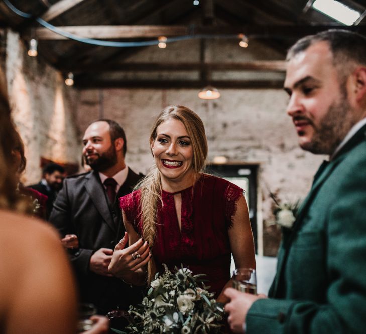 Bridesmaid in Maroon ASOS Dress with Lace Cap Sleeves, Halterneck and Leg Split | Wedding Bouquet of White Flowers and Green Foliage with White Trailing Ribbon | Bride in Anne Priscilla Signature Gown with Halterneck, Keyhole Back and Belt | Floor Length Veil | Groom in Mackintosh Tartan Red and Black Kilt with Green Jacket and Waistcoat | Kinkell Byre Wedding Venue | Festoon Light Canopy and Indoor Trees for Humanist Wedding in St Andrews | Carla Blain Photography