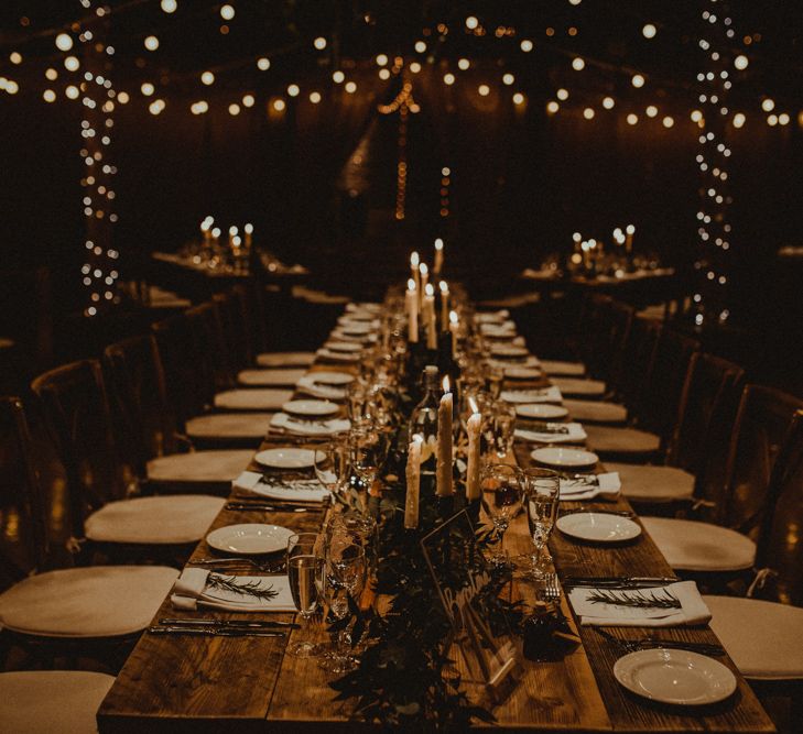 Wooden Banquet Table | Foliage Table Runner | White Tapered Candles | Perspex Table Sign | Rosemary Sprig Place Setting | Kinkell Byre Wedding Venue | Festoon Light Canopy and Indoor Trees for Humanist Wedding in St Andrews | Carla Blain Photography