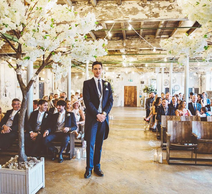 Groom Waiting at Altar | Groom in Navy Tails and Grey Waistcoat | Cherry Blossom Tree Altar | Festoon Lights | Lace Bridal Cape Veil &amp; Fishtail Wedding Dress by Pronovias | On Love and Photography