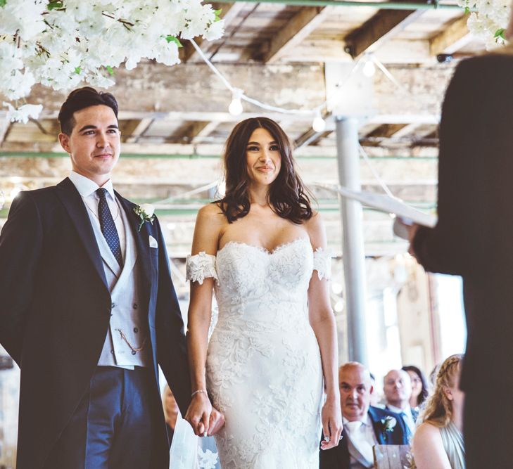 Wedding Ceremony | Bride in Fishtail Pronovias Wedding Dress with Off Shoulder Sleeves and Veil Cape | Groom in Navy Tails and Grey Waistcoat | Bride Wearing Hair Down | Cherry Blossom Tree Altar | Lace Bridal Cape Veil &amp; Fishtail Wedding Dress by Pronovias | On Love and Photography