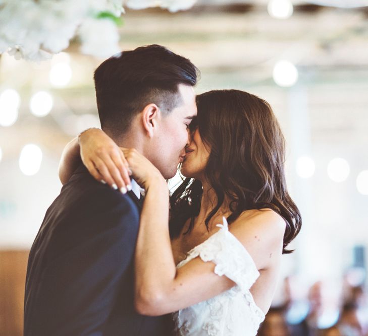 First Kiss | Bride in Embroidered Pronovias Wedding Dress with Off Shoulder Sleeves and Veil Cape | Groom in Navy Tails and Grey Waistcoat | Bride Wearing Hair Down | Lace Bridal Cape Veil &amp; Fishtail Wedding Dress by Pronovias | On Love and Photography