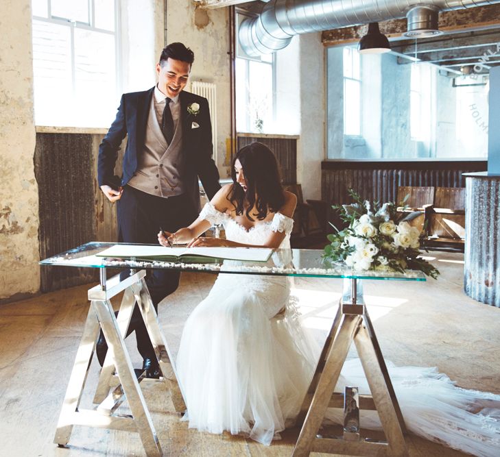 Signing of Register | Bride in Fishtail Pronovias Wedding Dress with Off Shoulder Sleeves and Veil Cape | Groom in Navy Tails and Grey Waistcoat | Bride Wearing Hair Down | Bridal Bouquet of White Roses and Greenery | Lace Bridal Cape Veil &amp; Fishtail Wedding Dress by Pronovias | On Love and Photography