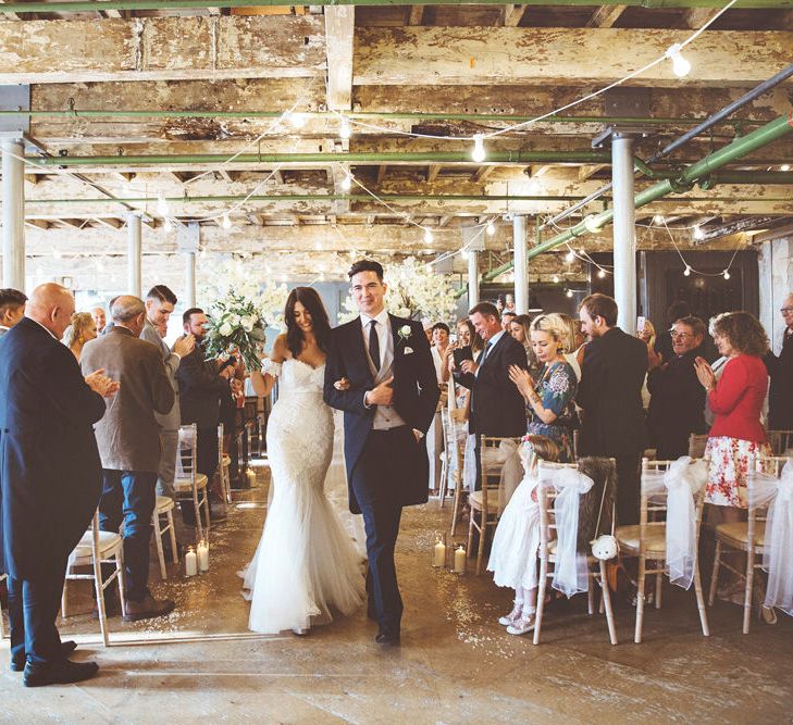 Just Married | Bride in Fishtail Pronovias Wedding Dress with Off Shoulder Sleeves and Veil Cape | Groom in Navy Tails and Grey Waistcoat | Bride Wearing Hair Down | Bridal Bouquet of White Roses and Greenery | Cherry Blossom Tree Altar | Festoon Lights | Pillar Candles | Aisle Petals | Lace Bridal Cape Veil &amp; Fishtail Wedding Dress by Pronovias | On Love and Photography