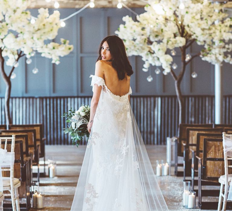 Bride in Embroidered Pronovias Wedding Dress with Off Shoulder Sleeves and Veil Cape | Bride Wearing Hair Down | Bridal Bouquet of White Roses and Greenery | Cherry Blossom Tree Altar | Festoon Lights | Pillar Candles | Aisle Petals | Lace Bridal Cape Veil &amp; Fishtail Wedding Dress by Pronovias | On Love and Photography