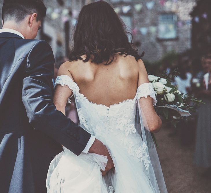 Bride in Fishtail Pronovias Wedding Dress with Off Shoulder Sleeves and Veil Cape | Groom in Navy Tails and Grey Waistcoat | Bride Wearing Hair Down | Bridal Bouquet of White Roses and Greenery | Wedding Bunting | Lace Bridal Cape Veil &amp; Fishtail Wedding Dress by Pronovias | On Love and Photography