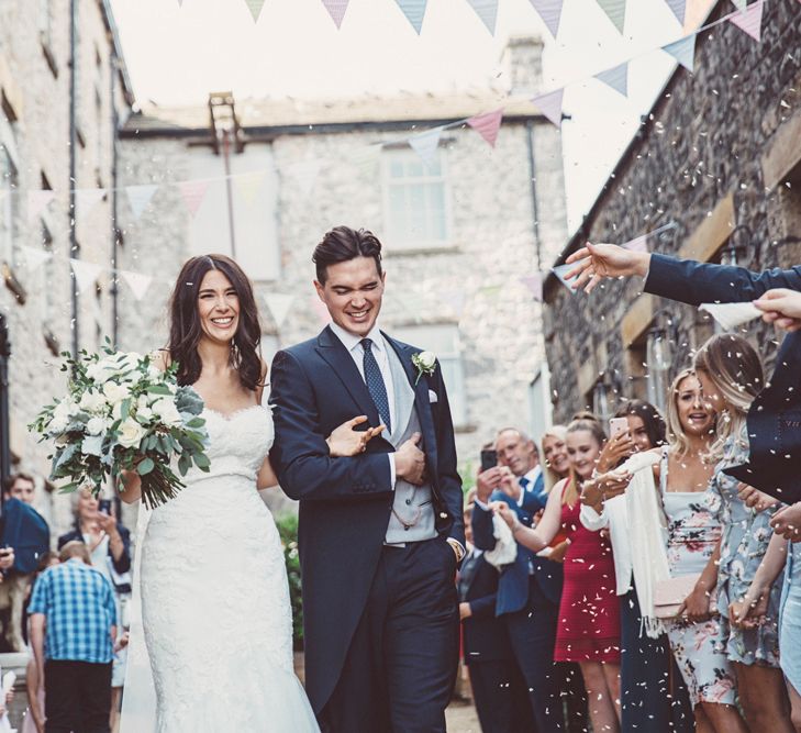 Confetti Throw | Bride in Embroidered Pronovias Wedding Dress with Off Shoulder Sleeves and Veil Cape | Groom in Navy Tails and Grey Waistcoat | Bride Wearing Hair Down | Bridal Bouquet of White Roses and Greenery | Wedding Bunting | Lace Bridal Cape Veil &amp; Fishtail Wedding Dress by Pronovias | On Love and Photography