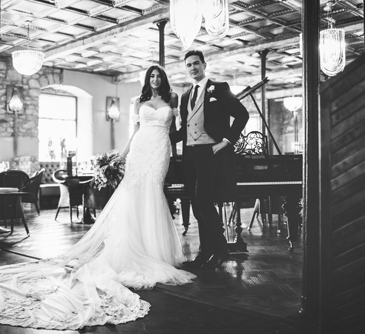 Bride in Fishtail Pronovias Wedding Dress with Off Shoulder Sleeves and Veil Cape | Groom in Navy Tails and Grey Waistcoat | Bride Wearing Hair Down | Bridal Bouquet of White Roses and Greenery | Lace Bridal Cape Veil &amp; Fishtail Wedding Dress by Pronovias | On Love and Photography