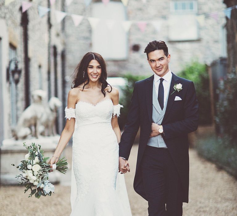 Bride in Fishtail Pronovias Wedding Dress with Off Shoulder Sleeves and Veil Cape | Groom in Navy Tails and Grey Waistcoat | Bride Wearing Hair Down | Bridal Bouquet of White Roses and Greenery | Lace Bridal Cape Veil &amp; Fishtail Wedding Dress by Pronovias | On Love and Photography