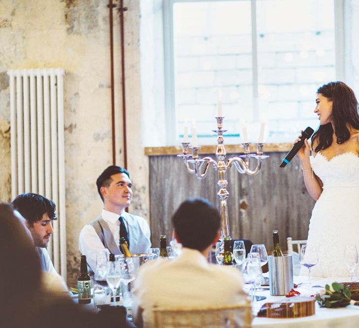 Bride's Speech | Bride in Fishtail Pronovias Wedding Dress with Off Shoulder Sleeves and Veil Cape | Groom in Navy Tails and Grey Waistcoat | Gold Candleabra with White Tapered Candles | Bride Wearing Hair Down | Exposed Copper Piping | Lace Bridal Cape Veil &amp; Fishtail Wedding Dress by Pronovias | On Love and Photography