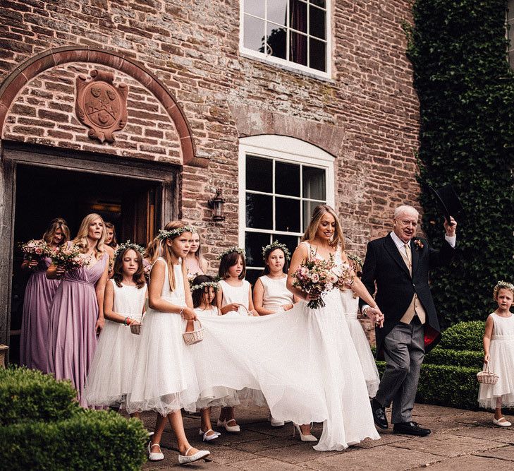 Bride with bridesmaids makes her way to church ceremony at Dewsall Court