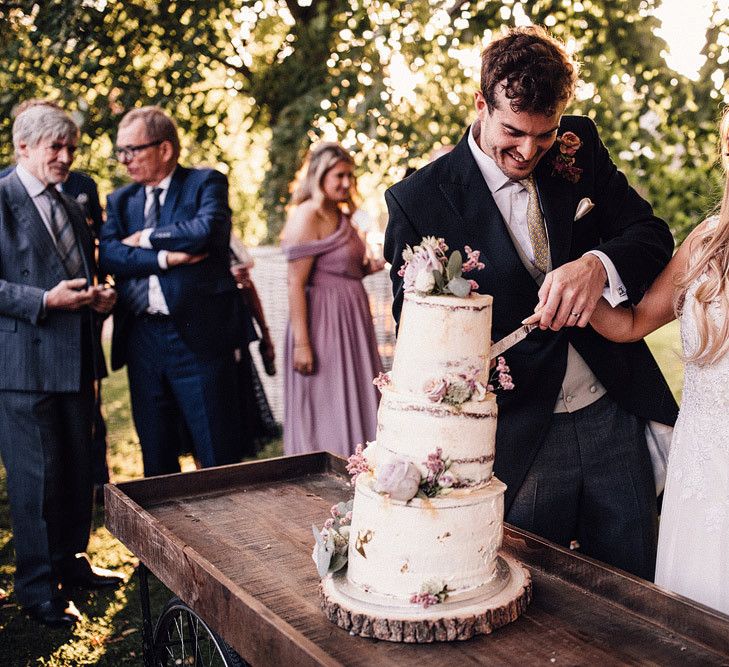 Bride and groom cut rustic wedding cake on tree slice cake stand