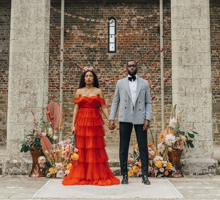 Stylish bride and groom in red dress and grey blazer at Chiddingstone Castle