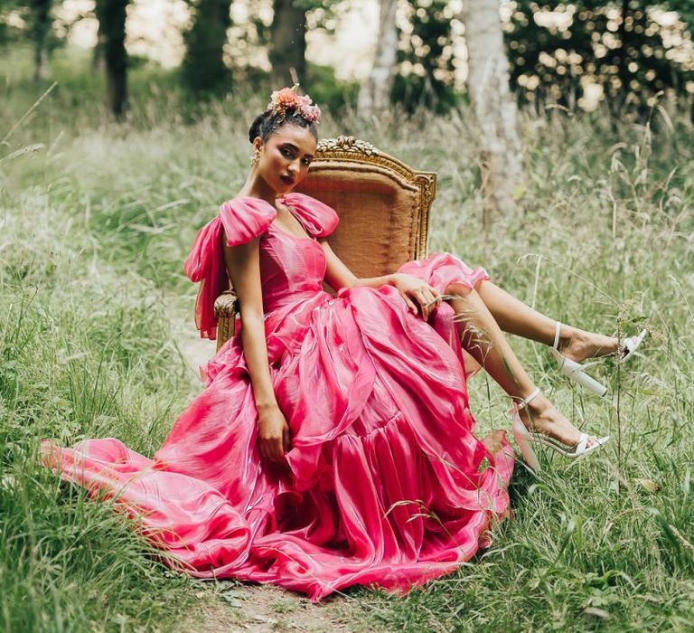 bride in pink wedding dress sitting on a chair in the woods at Chiddingstone Castle