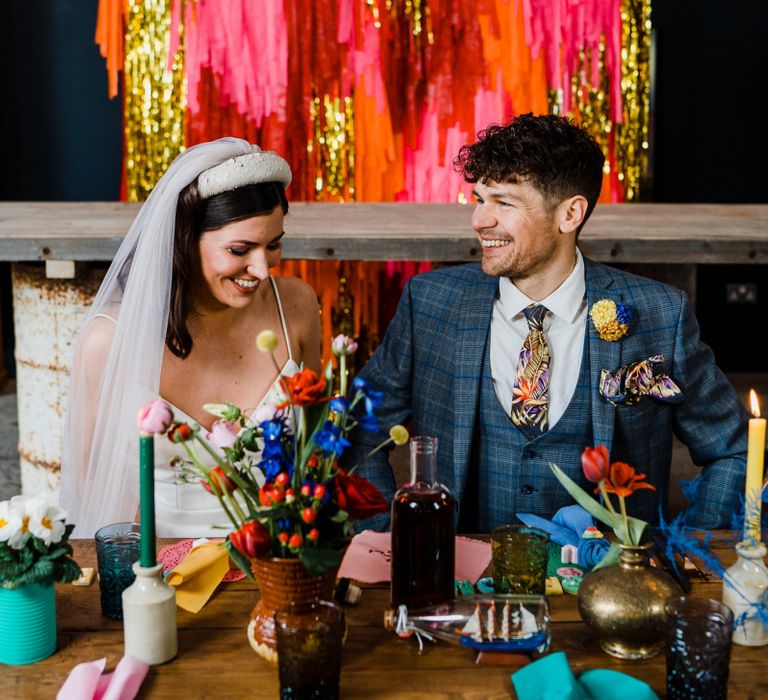 Bride and groom sitting at the reception table with tassle backdrop