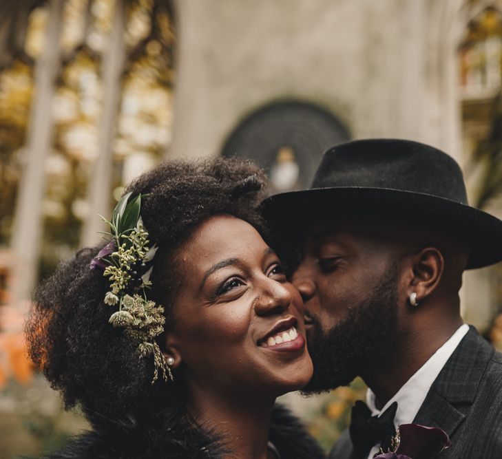 Stylish groom in hat kissing his bride with flower in her hair