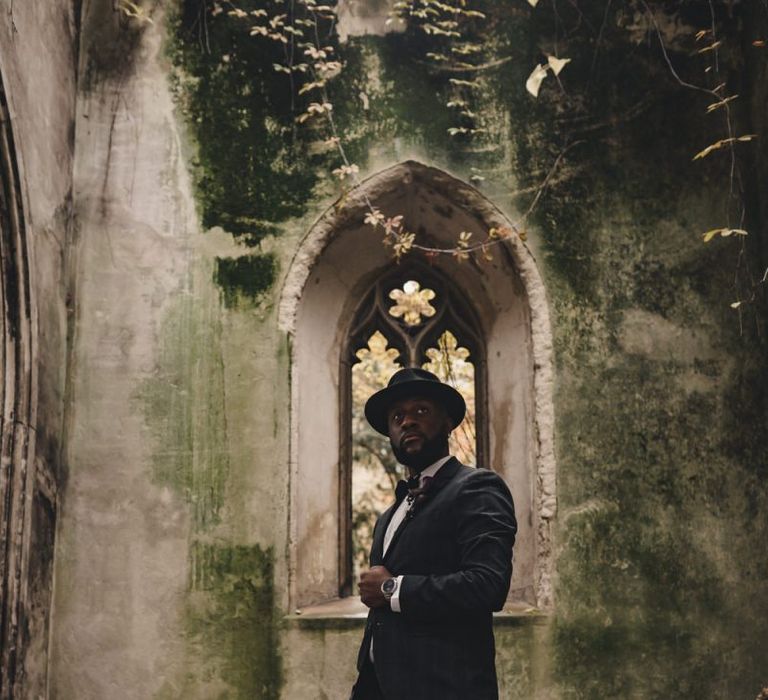 Stylish groom in black suit, bow tie and hat for city wedding