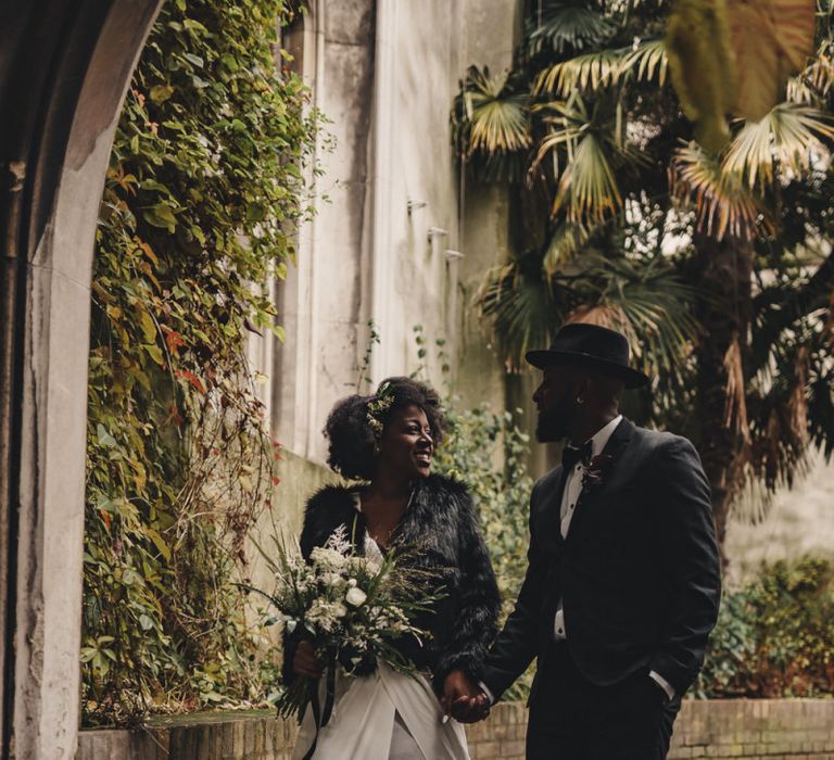 Stylish bride and groom walking through the St Dunstan in the East church gardens