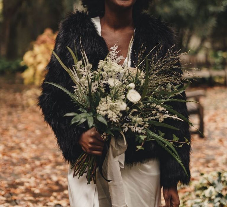 Black bride in faux fur coverup holding a green and white wedding bouquet  tied with ribbon