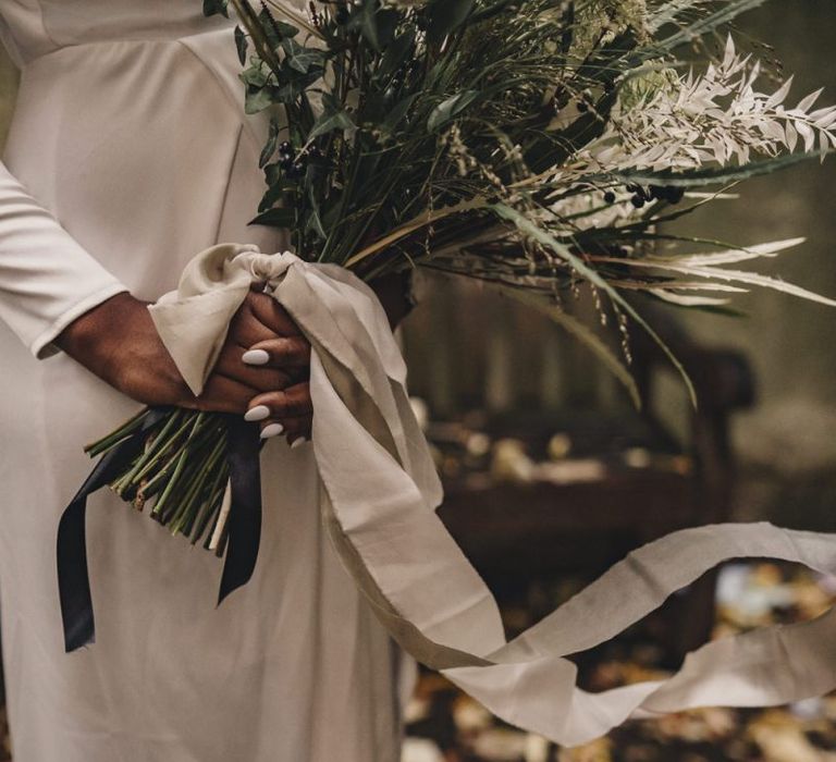 Black bride with white nail polish holding wedding bouquet tied with ribbon