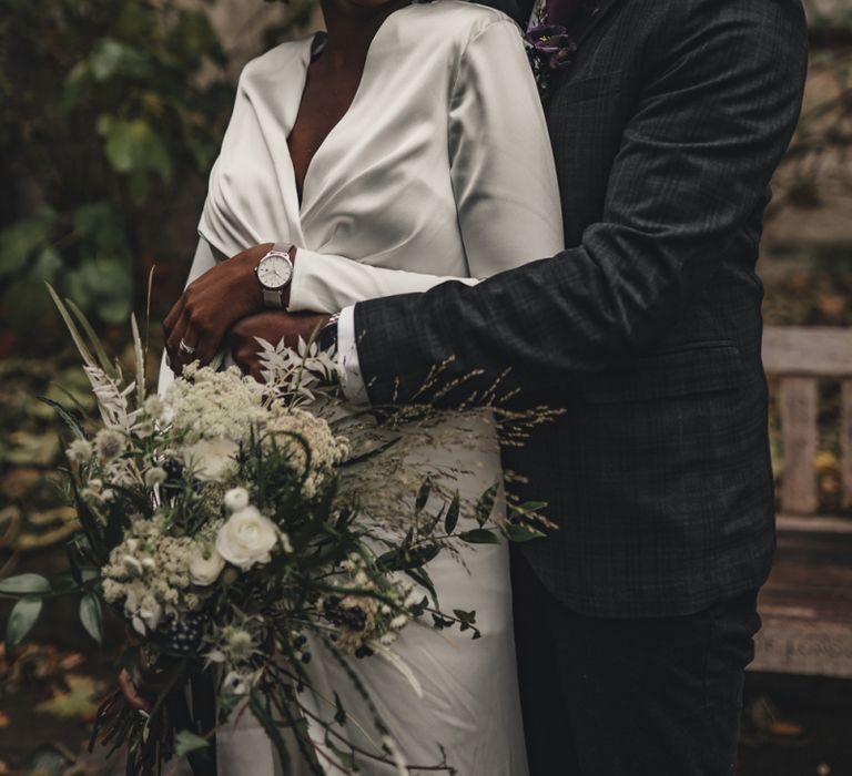 Groom in bow tie and hat embracing his bride with wrap satin dress