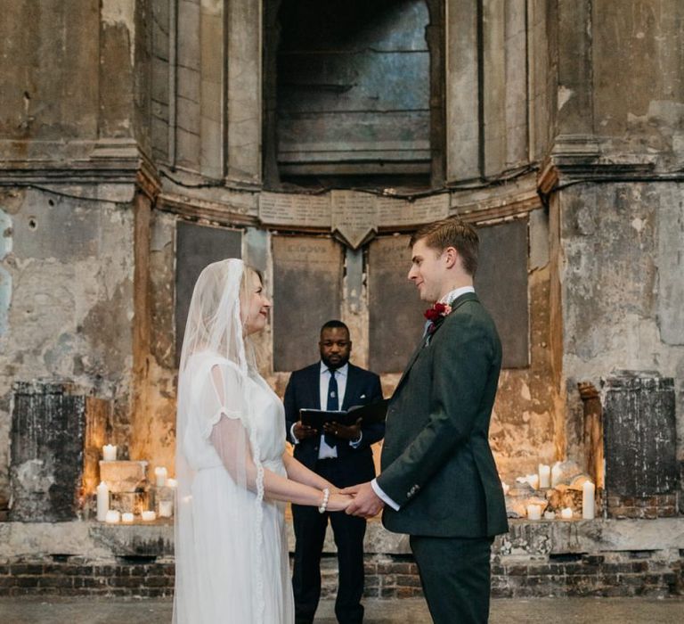 Bride wearing a sophisticated dress with lace tipped veil with her groom at London wedding  with candle light backdrop