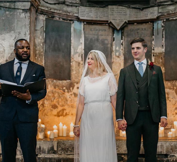 Bride wearing a  lace tipped veil with her groom at London wedding  with candle light backdrop