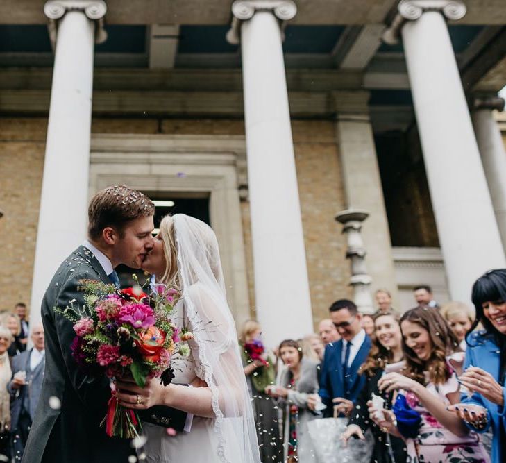 Bride and groom embrace with bright and colour bouquet for a fun and eclectic day