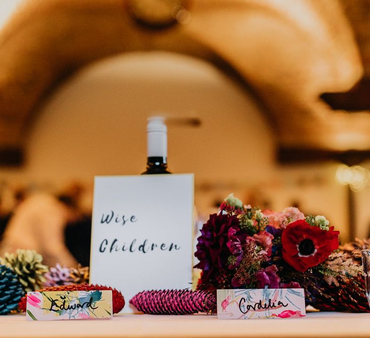 Hand painted watercolour place cards with pine cone wedding decor and bright flower arrangements