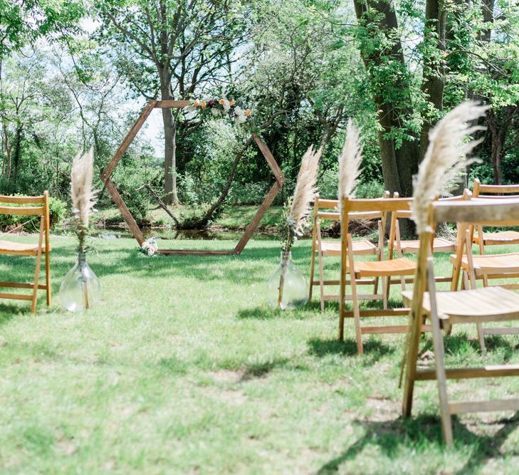 Outdoor Wedding Ceremony Set up with Wooden Chairs Decorated with Pampas Grass and Hexagonal Altar