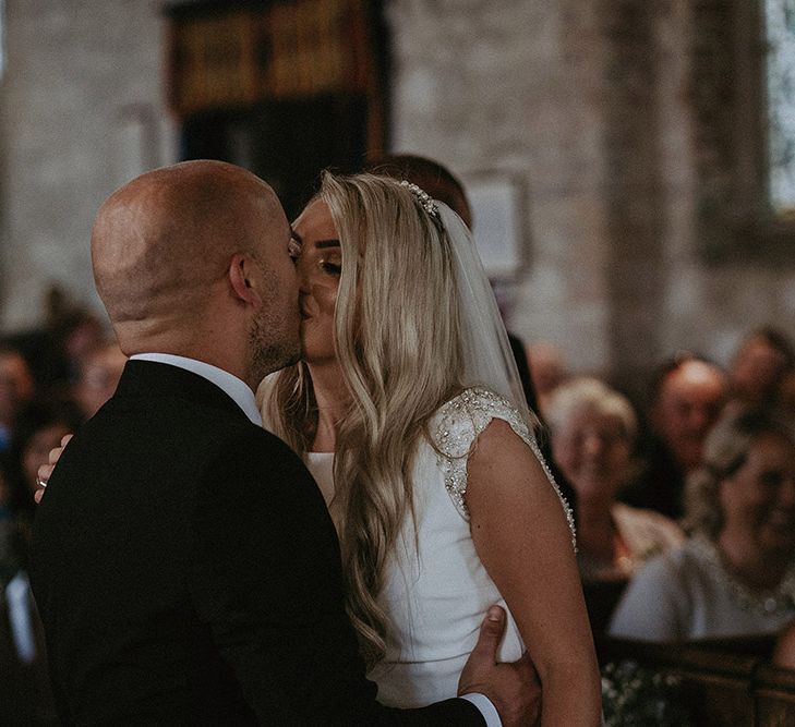 Church Wedding Ceremony with Bride in St Patrick Wedding Dress and Groom in Dark Suit Kissing