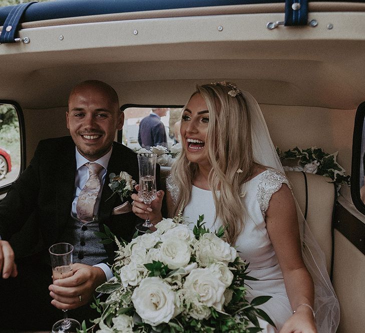 Bride in St Patrick Wedding Dress and Groom in Dark Suit Sitting in Classic Wedding Car