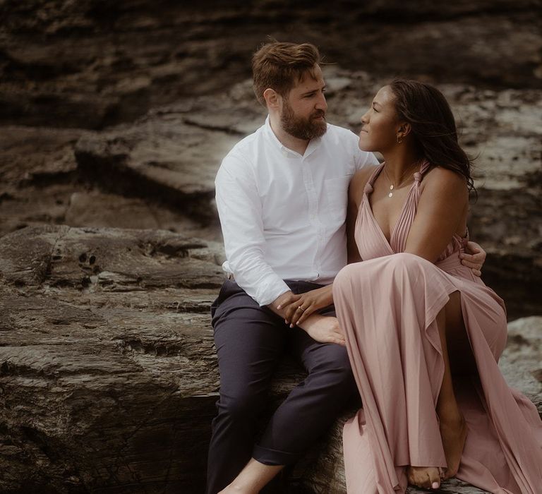 Bride and groom sitting on the rocks at their beach engagement session