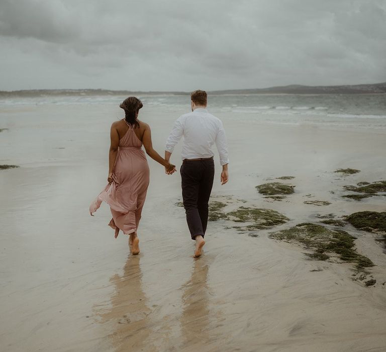 Bride and groom-to-be walking in the surf at Cornwall beach engagement session