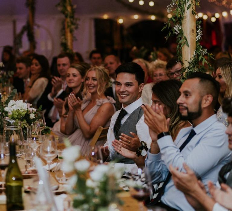 Guests enjoy wedding speeches with fairy lights in marquee