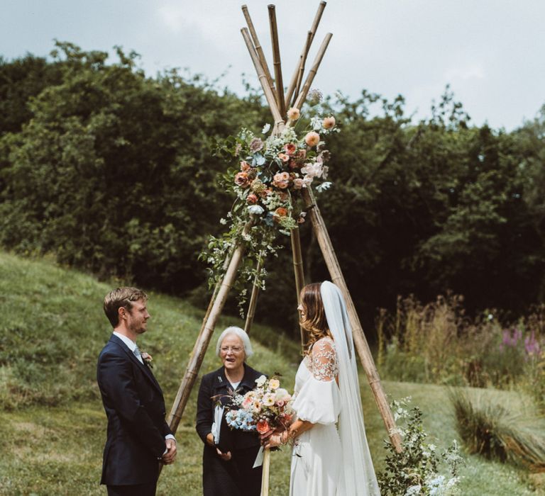 Outdoor Wedding Ceremony in Front of Naked Tipi  Decorated in Pastel Flowers