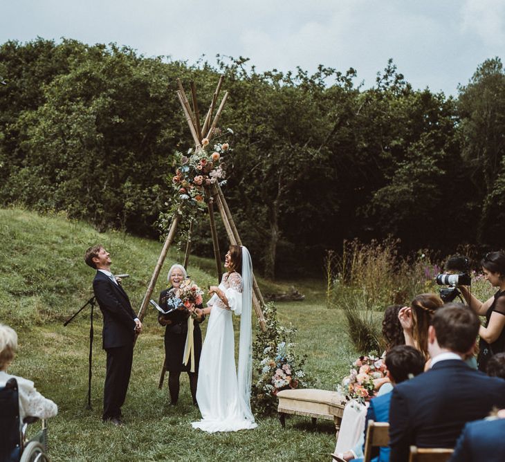 Bride in Rime Arodaky Wedding Dress and Groom is Reiss Suit at Outdoor Wedding Ceremony with Naked Tipi Altar