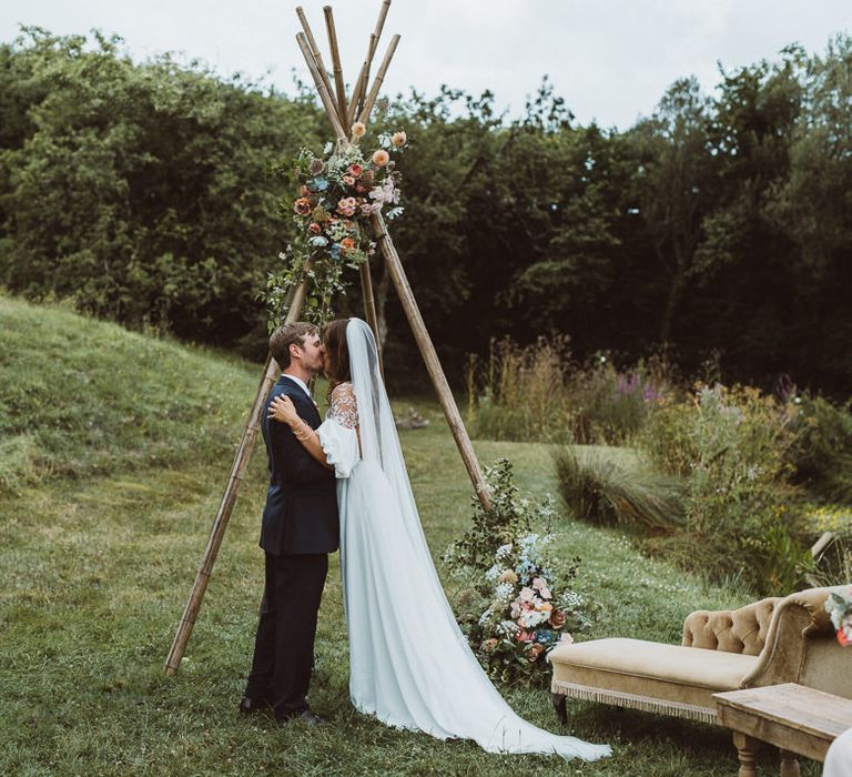 Bride in Rime Arodaky Wedding Dress and Groom is Reiss Suit at Outdoor Wedding Ceremony with Naked Tipi Altar