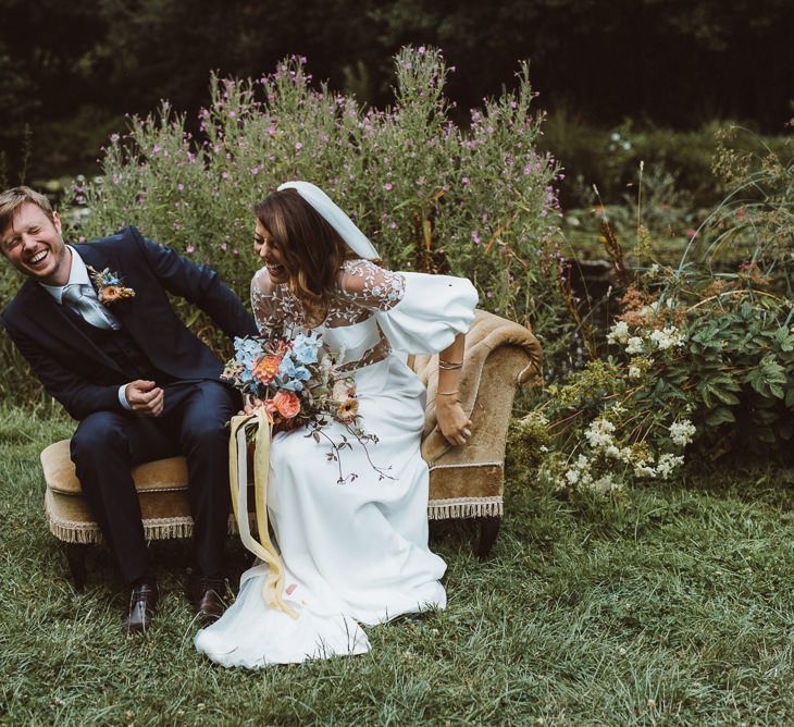 Bride in Rime Arodaky Wedding Dress and Groom is Reiss Suit Sitting on a Vintage Chaise Lounge During Outdoor Wedding Ceremony