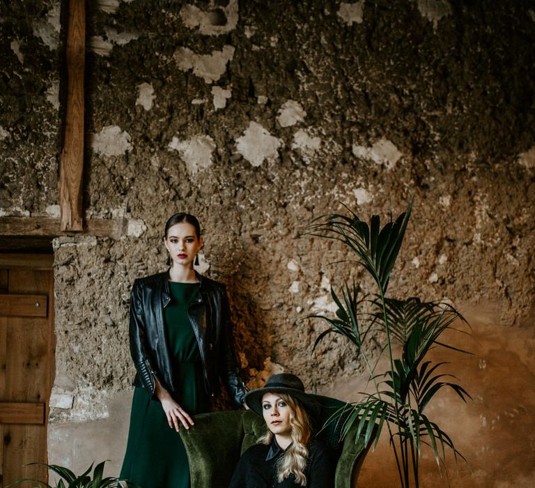 Green Velvet Chair | Botanical Plants | Bride in Black Dress &amp; Leather Jacket | Bridesmaid in Forest Green Dress &amp; Leather Jacket | Forest Green and Black Dark Decadence Wedding Inspiration in a Rustic Barn Planned &amp; Styled by Knots &amp; Kisses with Images by Daze of Glory Photography