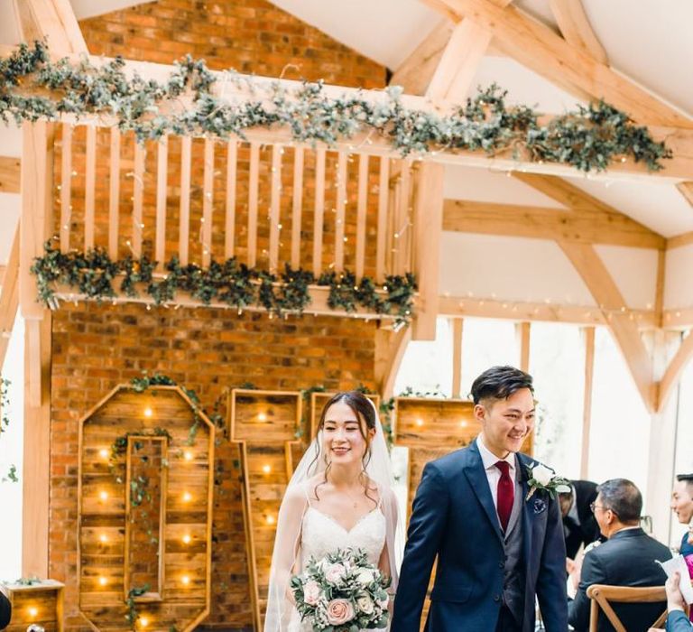 Bride and groom tie the knot with wooden Love sign decorated with green foliage and lanterns